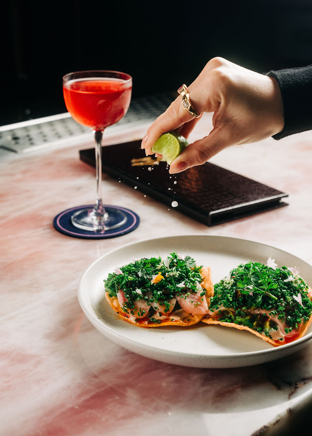 Himachi crudo tostada with a hand squeezing a lime over it and a cocktail off to the side