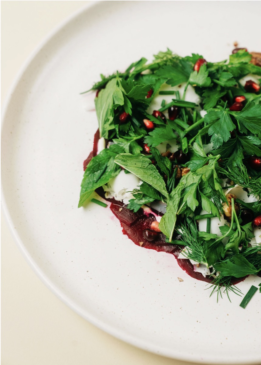 Beet carpaccio salad with mint and pomegranate seeds on a white plate