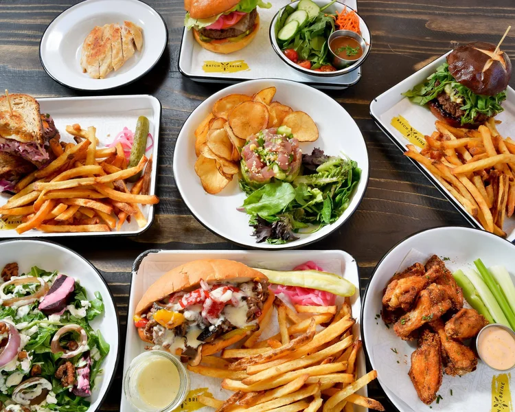 Assorted meals including burgers, salads, chicken wings, tacos, and dumplings on a table.