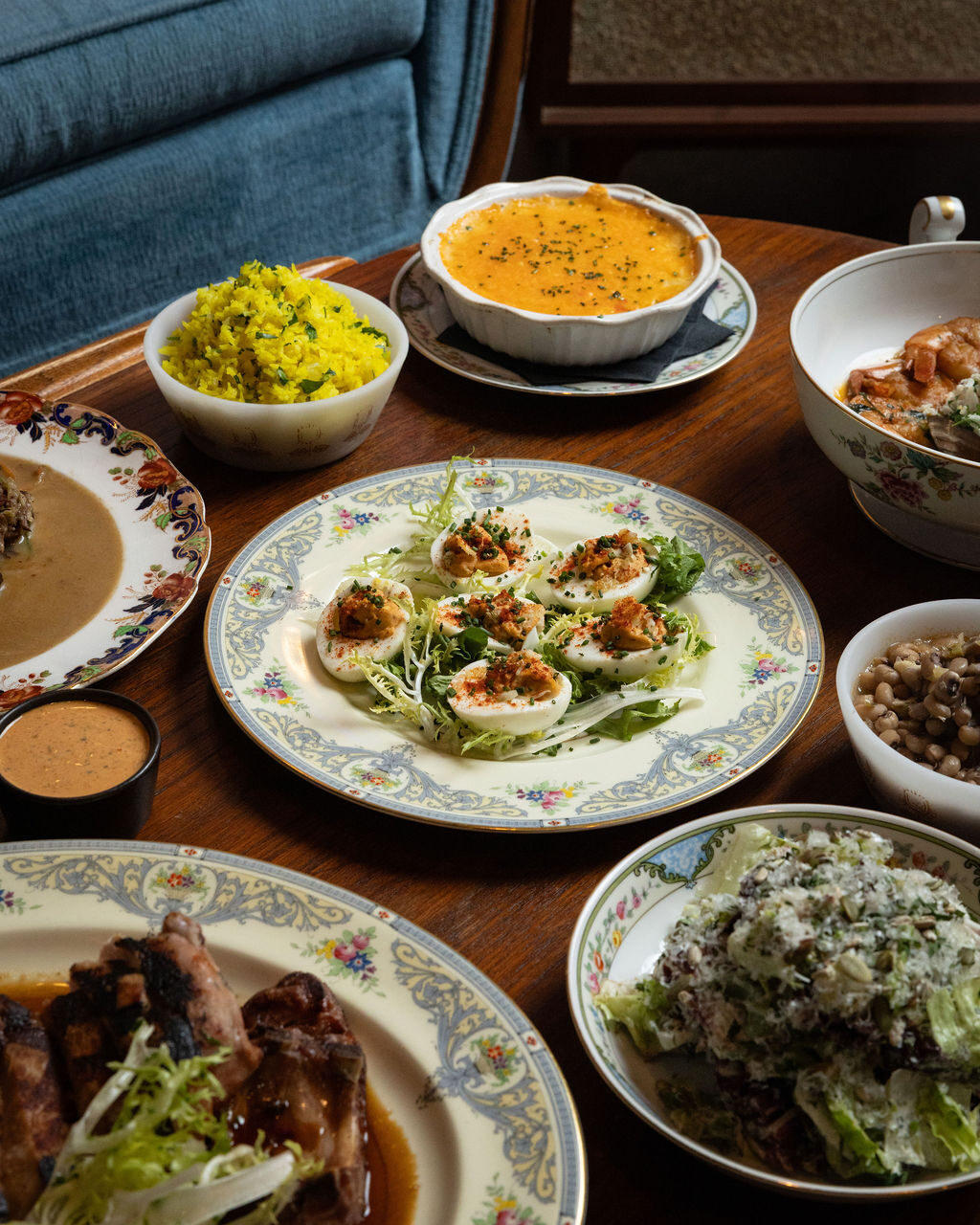 Table spread with deviled eggs, yellow rice, black-eyed peas, salad, and grilled pork chop on vintage china